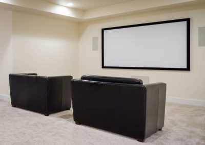 A room with two black leather chairs and a projector screen.