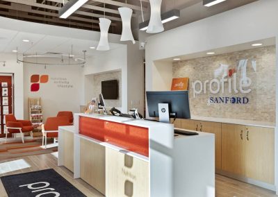 A reception area with orange chairs and white counters.